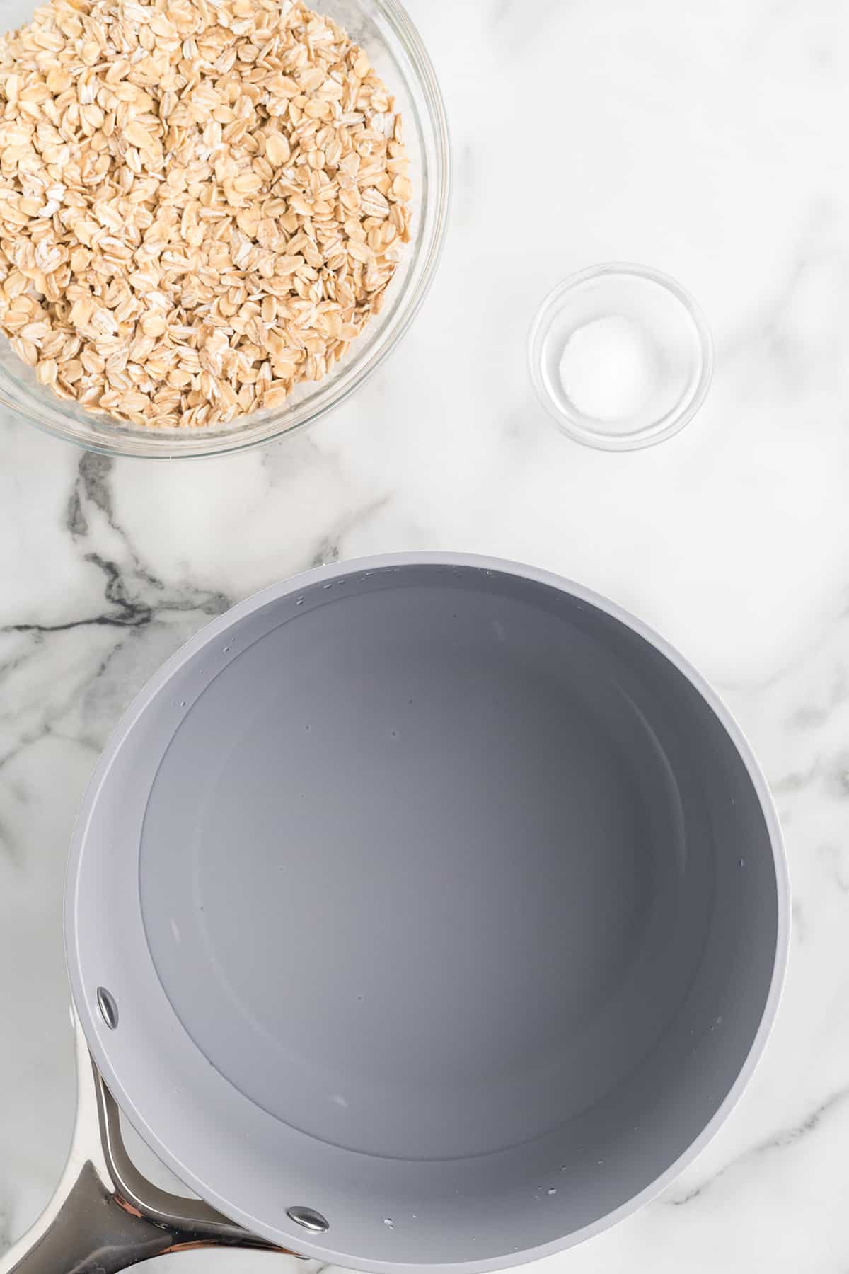 A saucepan with water and salt; a bowl of rolled oats in the background.
