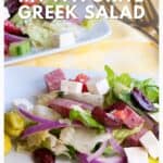 A plate of Greek salad with feta, olives, red onions, pepperoncini, and lettuce on a white dish.