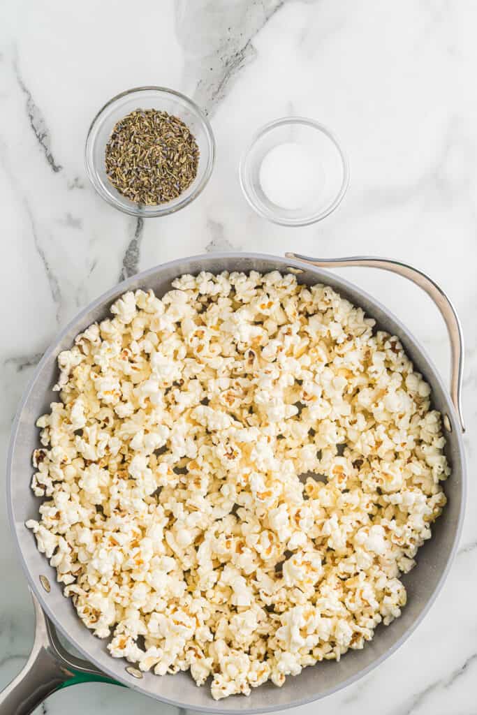 Popped corn in a skillet with herbs and salt set to the side.