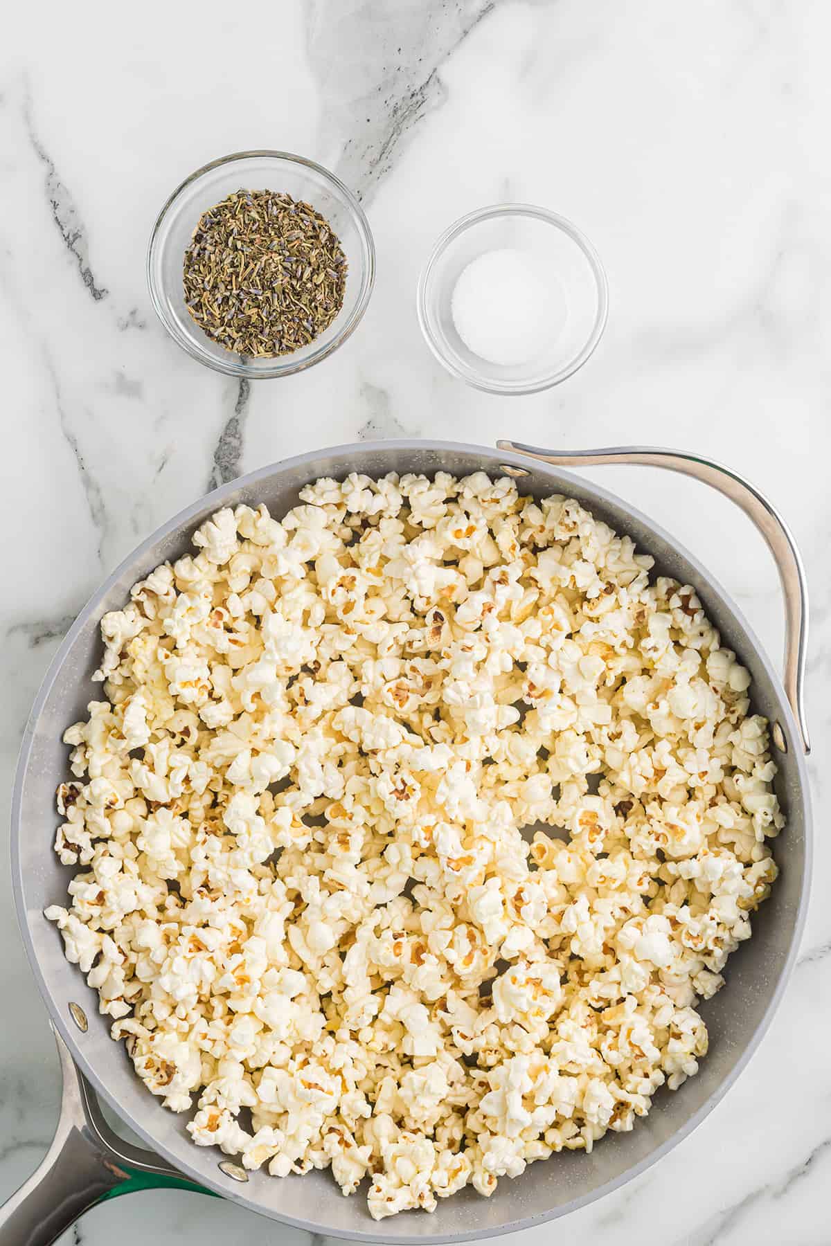 Popped corn in a skillet with herbs and salt set to the side.