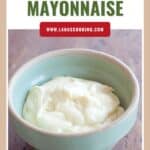 A green bowl filled with homemade mayonnaise sits on a wooden table.