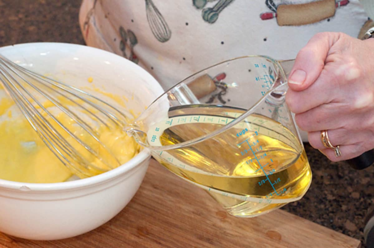Adding oil from a measuring cup into the mixing bowl.