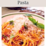 A bowl of tomato basil pasta topped with shredded cheese and fresh basil leaves.