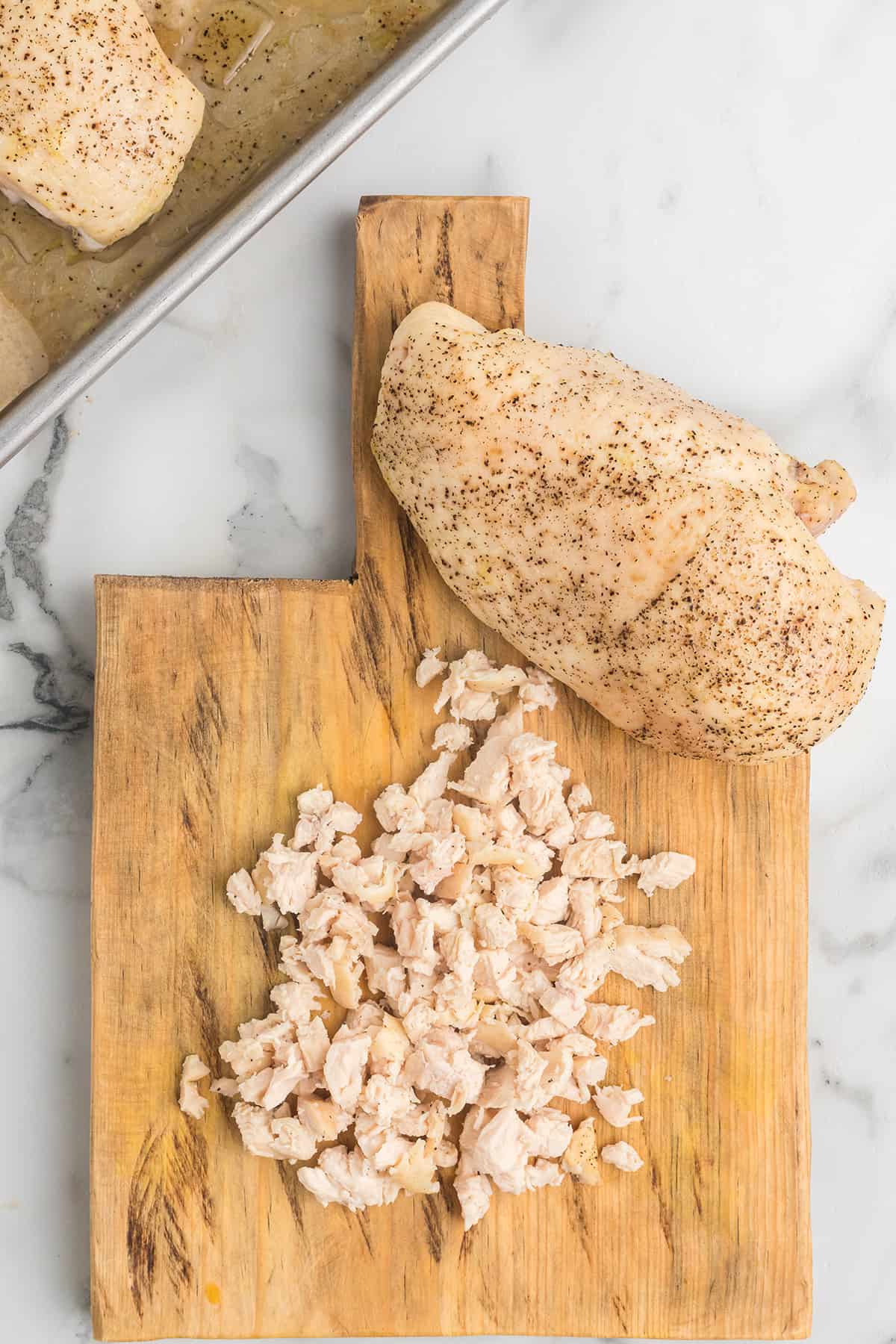 One whole chicken breasts and some chopped chicken on a cutting board.