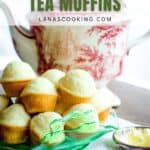 A stack of round, golden tea muffins sits on a green glass plate in front of a decorative teapot. A butter dish, a butter knife, and a white napkin are nearby. Text reads Easy Tea Muffins and lanascooking.com.