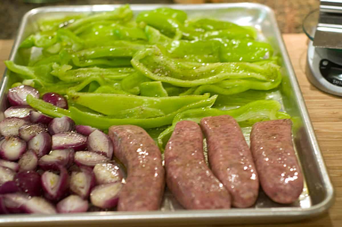 Prepped sausages, onions, and peppers on a baking sheet.