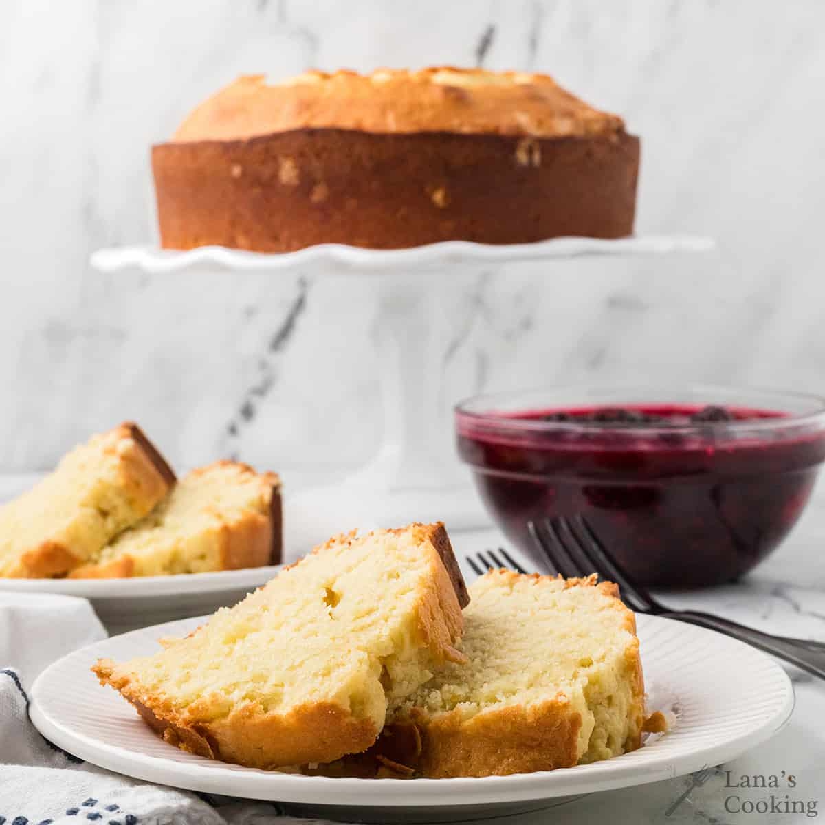 Slices of cake on a plate in front with finished pound cake on a pedestal in the background.