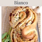 A braided loaf of Pane Bianco topped with sun-dried tomatoes and herbs on a cooling rack.
