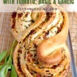 S-shaped braided bread with tomato, basil, and garlic on a cooling rack, fresh basil on the side.