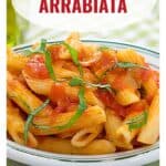A bowl of penne pasta arrabbiata topped with tomato sauce and fresh basil, with text and website link.