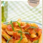 A plate of penne pasta arrabiata topped with tomato sauce and fresh basil on a green checkered tablecloth.