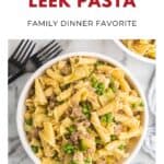 Bowl of sausage and leek pasta with peas, surrounded by forks, on a white marble surface.