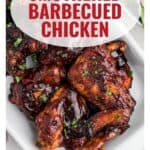 Barbecued chicken pieces with dark, glossy sauce on a white plate, garnished with parsley.