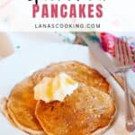 Two spiced pear pancakes with butter on a white plate, with a fork and floral napkin beside them.