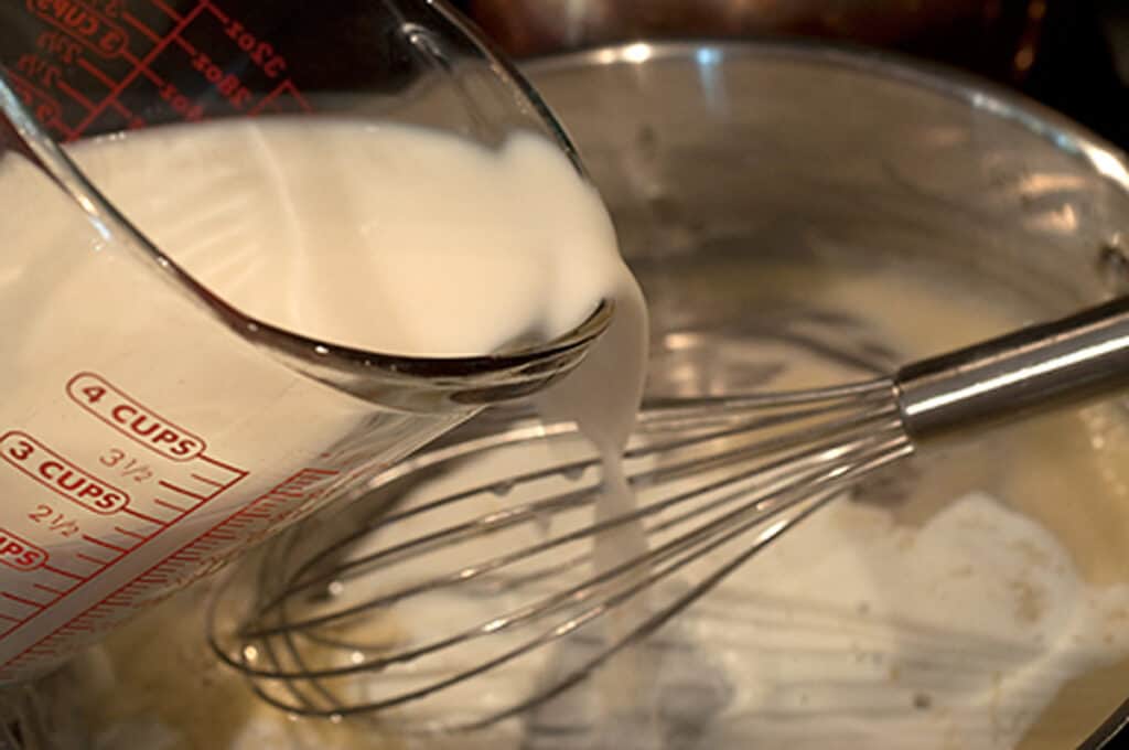 Milk being added to white roux to make a white sauce.