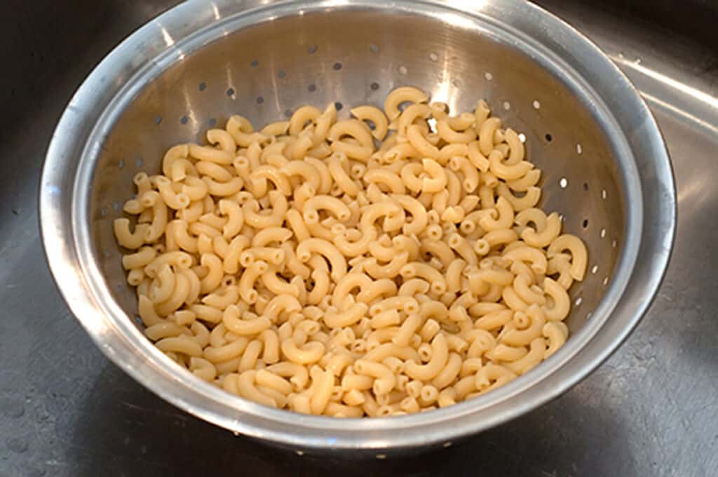 Cooked elbow macaroni draining in a colander.