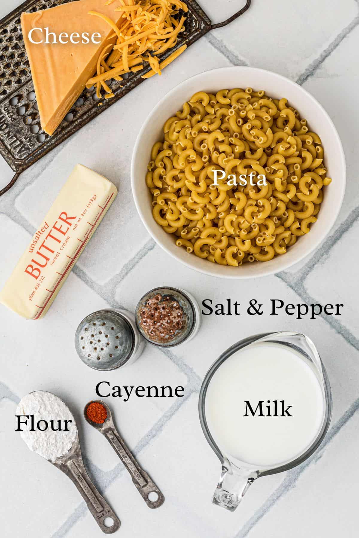 Ingredients for classic macaroni and cheese in separate containers on a tile background.