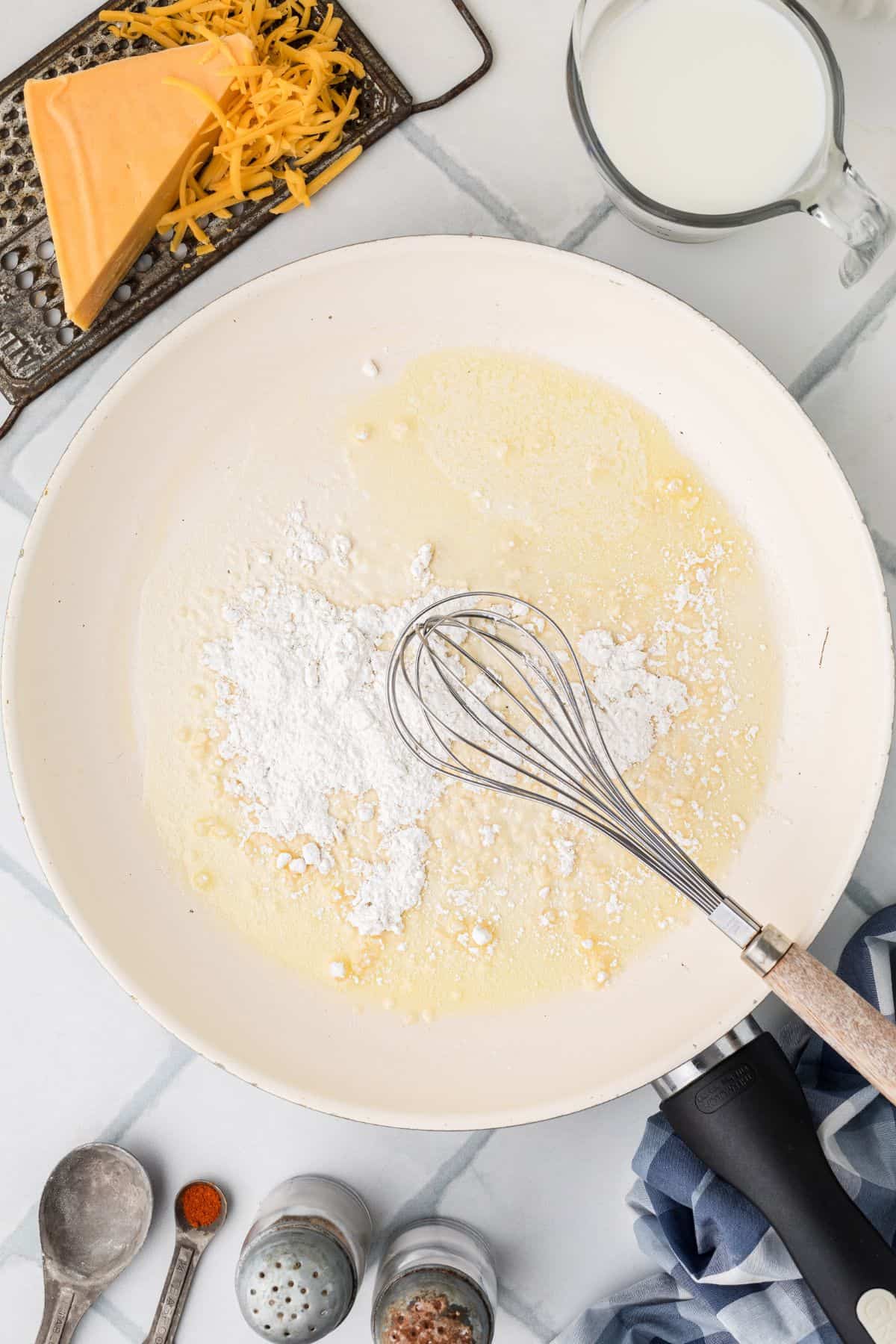 Flour being whisked into the melted butter on a tile background.