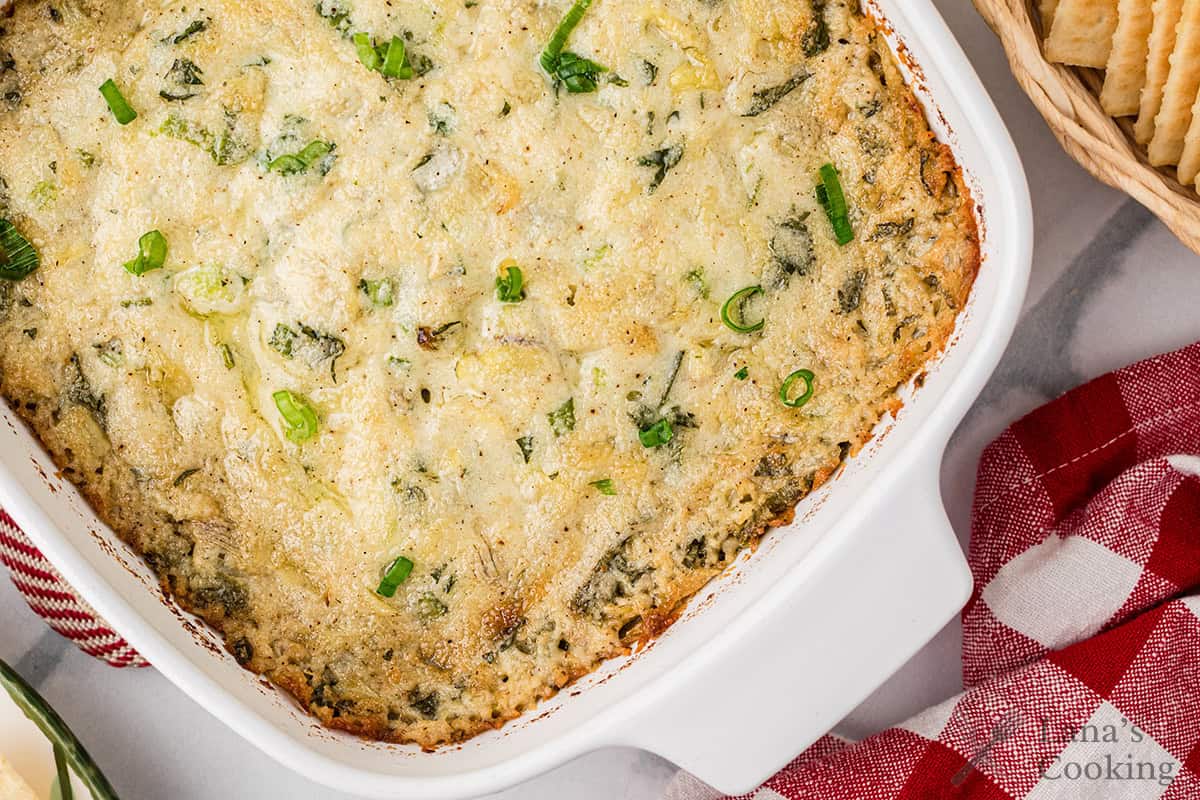 A baked spinach and artichoke dip in a white casserole dish, garnished with green onions.