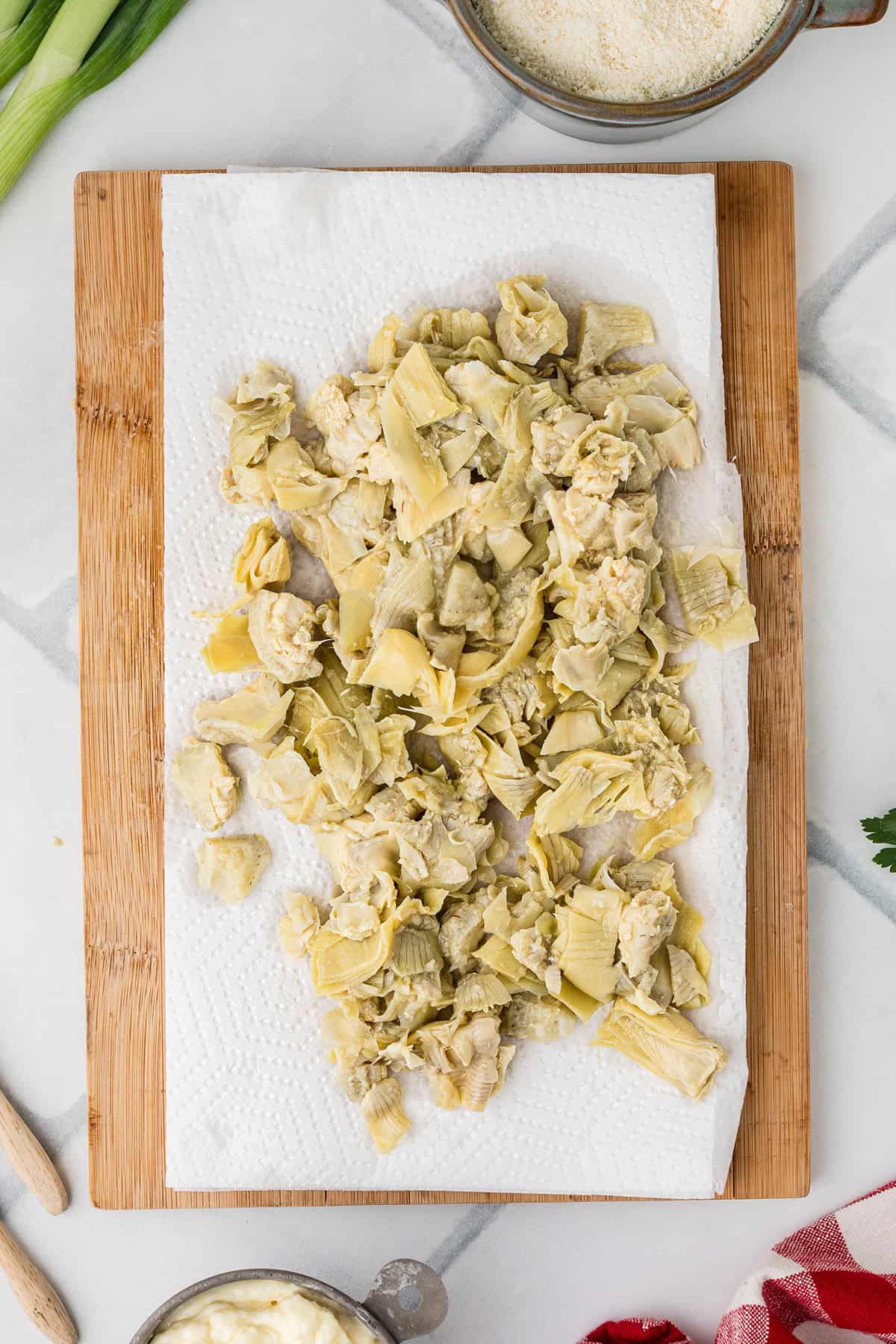 Chopped artichoke hearts draining on a paper towel-lined wooden cutting board.
