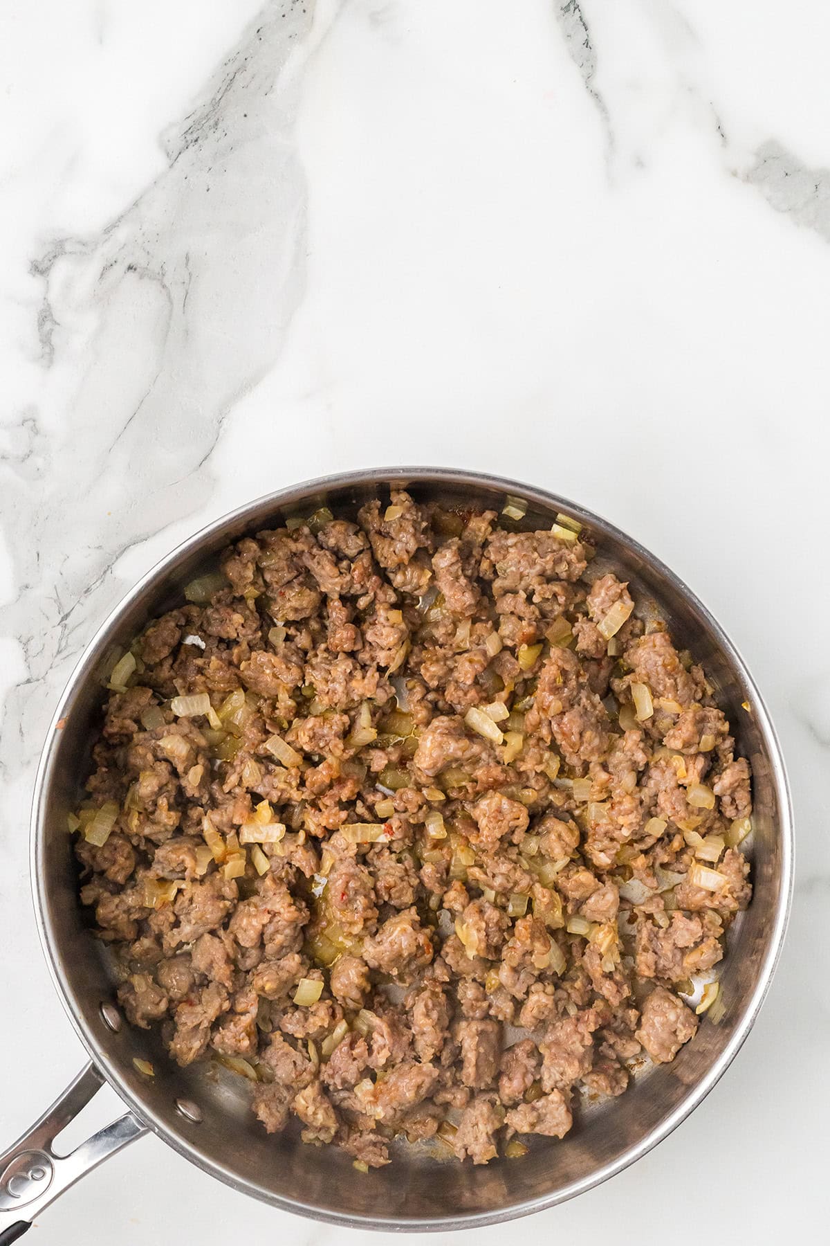 Ground beef and chopped onions cooking in a stainless steel skillet on a marble countertop.