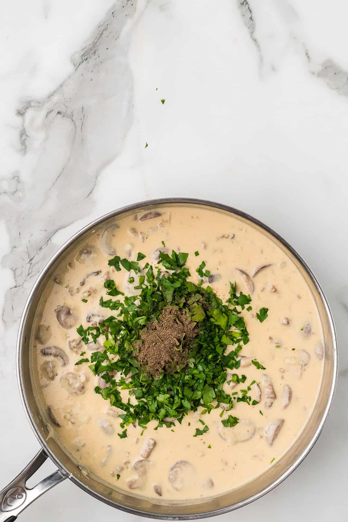 Creamy mushroom sauce in a pan, topped with chopped parsley and ground black pepper, on a marble surface.