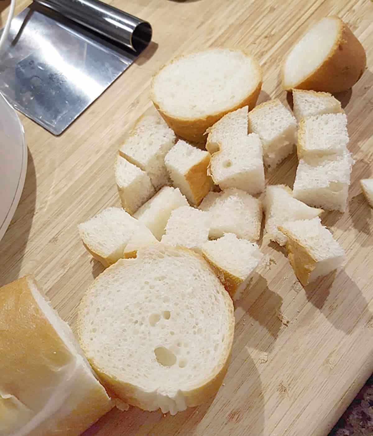 Sliced and cubed pieces of baguette bread on a wooden cutting board.
