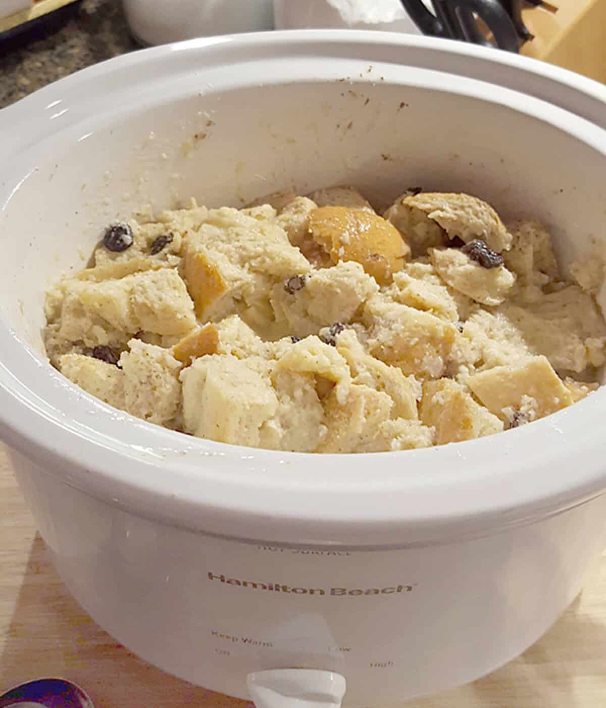 Crockpot filled with bread pudding mixture, including chunks of bread and raisins.