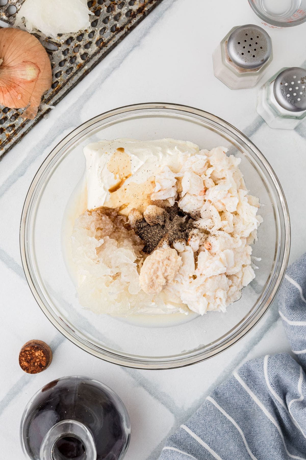 A glass bowl with crab meat, mayonnaise, seasonings, and horseradish on a white counter.
