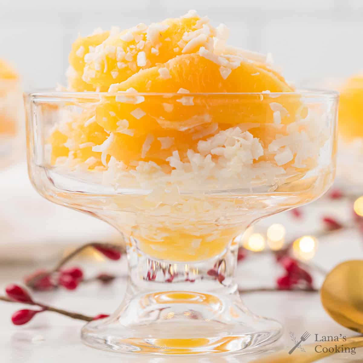 Glass dessert dish filled with orange segments and shredded coconut, with festive decor in the background.
