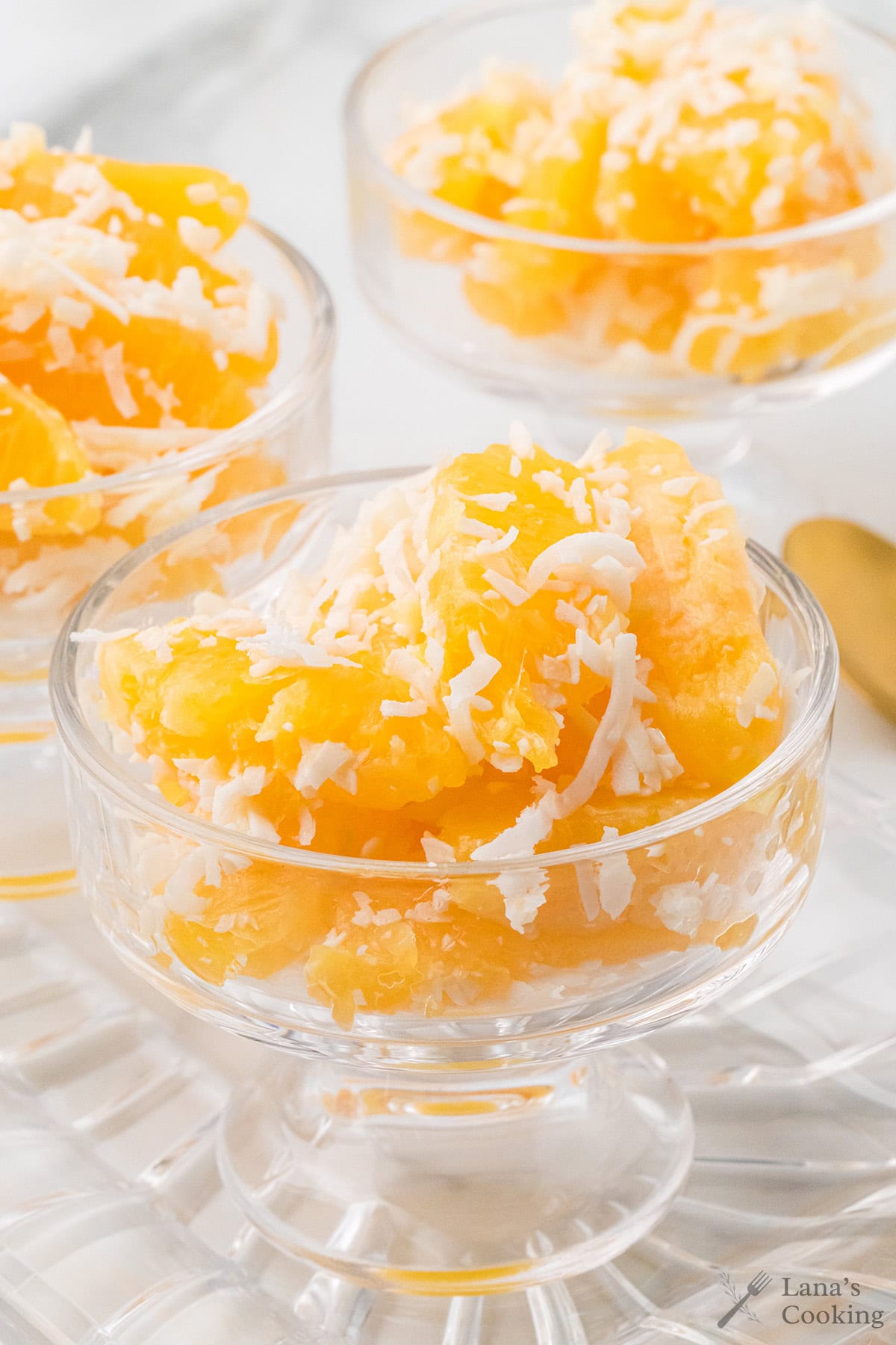 Glass bowls filled with orange segments topped with shredded coconut on a white surface.