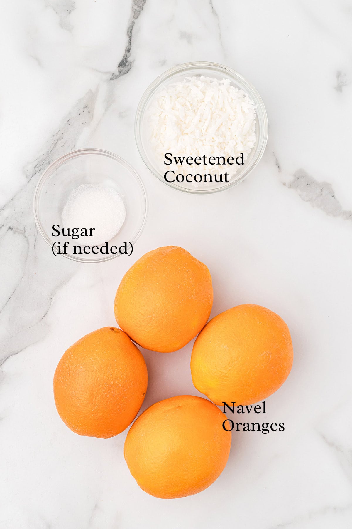 Four navel oranges, a bowl of sweetened coconut, and a bowl of sugar on a marble surface.