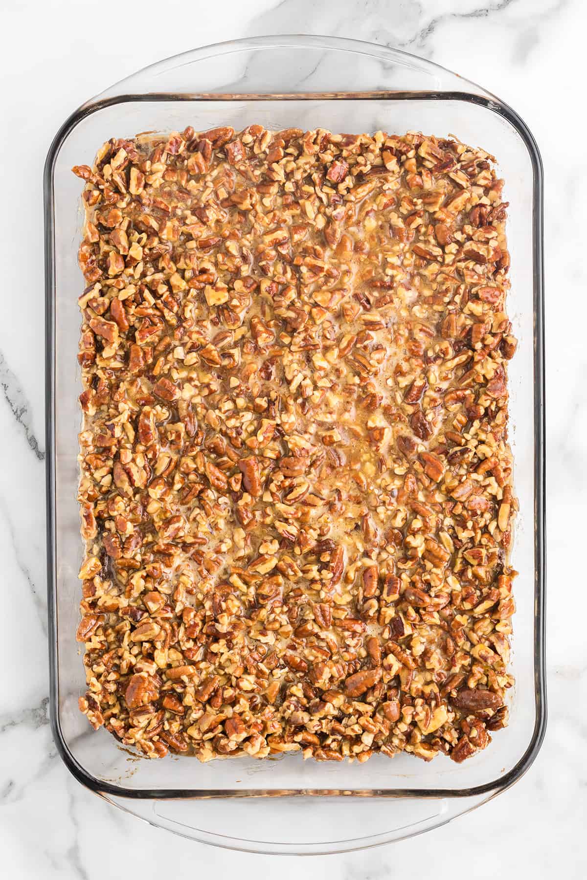A glass baking dish filled with a baked pecan dessert on a marble surface.