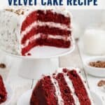 A sliced red velvet cake with white frosting on a cake stand, with a slice on a plate in front.