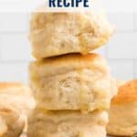 Three fluffy biscuits stacked on each other, with melted butter, and more biscuits in the background.