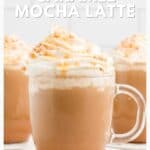 Glass mug of caramel mocha latte topped with whipped cream and caramel drizzle, with more mugs in background.
