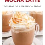A caramel mocha latte topped with whipped cream and caramel drizzle in a clear mug on a white plate.