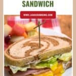Close-up of a ham and egg breakfast sandwich on swirled bread, with fruit salad in the background.