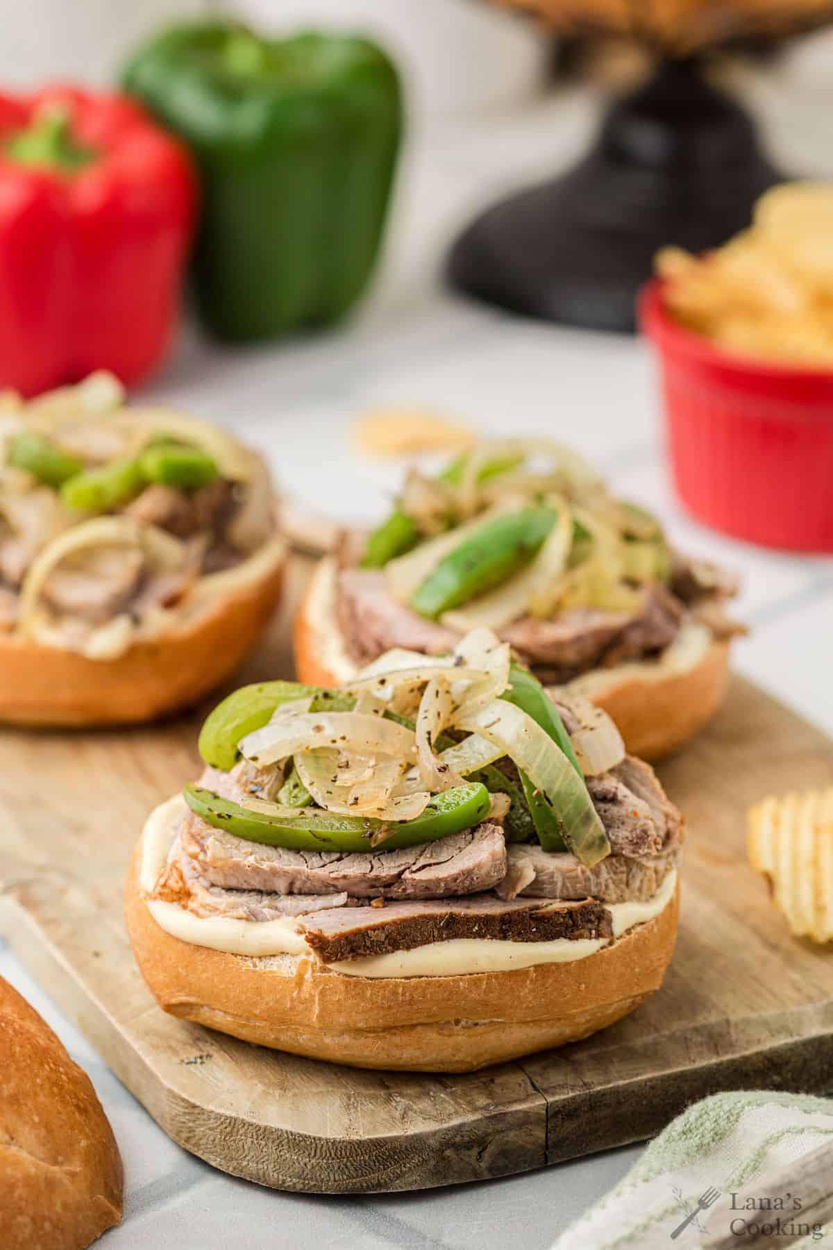 Pork tenderloin sandwiches on a wooden cutting board before being covered with the top bun.