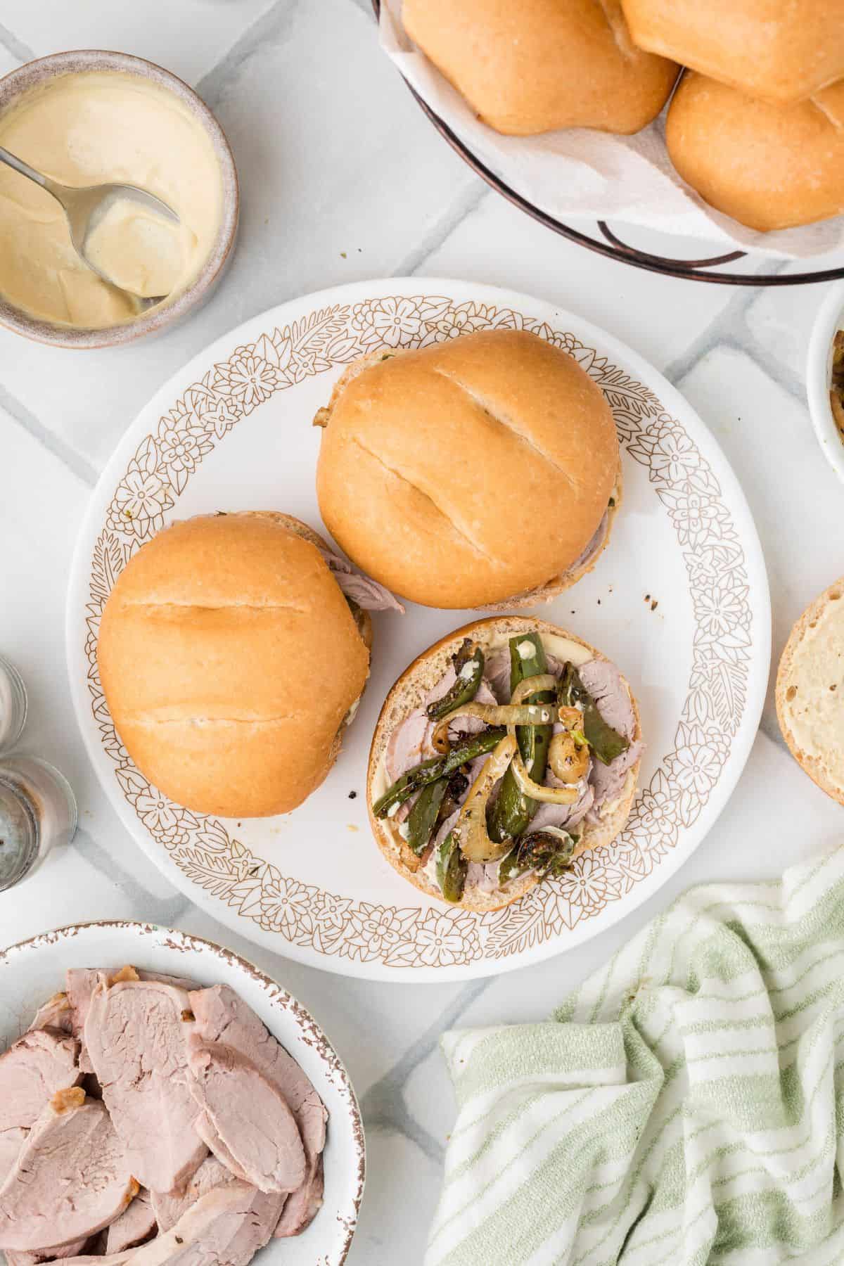 Roasted pork tenderloin sandwiches on a white plate with one sandwich uncovered.