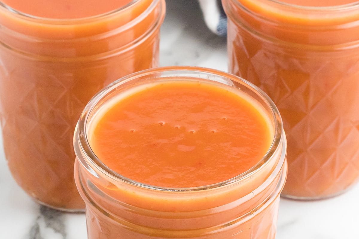 Three glass jars filled with barbecue sauce on a white surface.