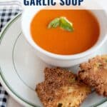 Bowl of tomato and roasted garlic soup with basil, served with crispy fritters on a plate.