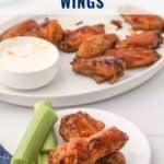 Plate of oven-baked buffalo wings with celery sticks and ranch dip, and more wings in the background.