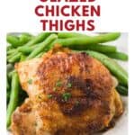 Chicken thigh with crispy golden skin, garnished with herbs, served with green beans on a white plate.