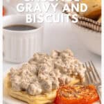 Biscuits topped with sausage gravy, a grilled tomato, and coffee on a white table with breakfast foods.