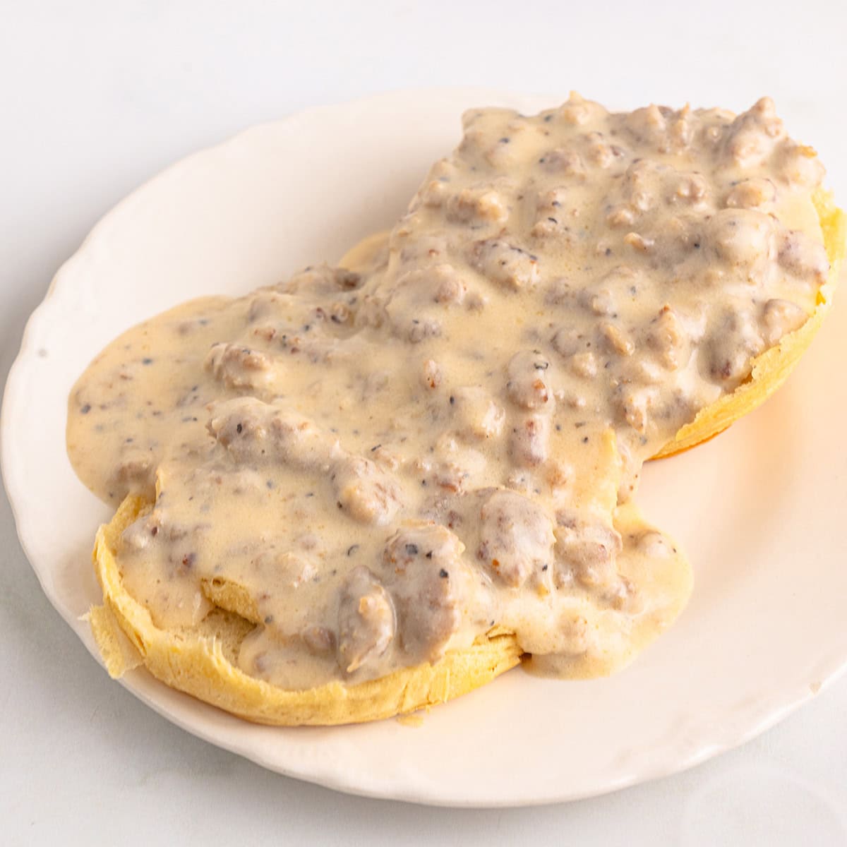 A biscuit topped with creamy sausage gravy on a white plate.