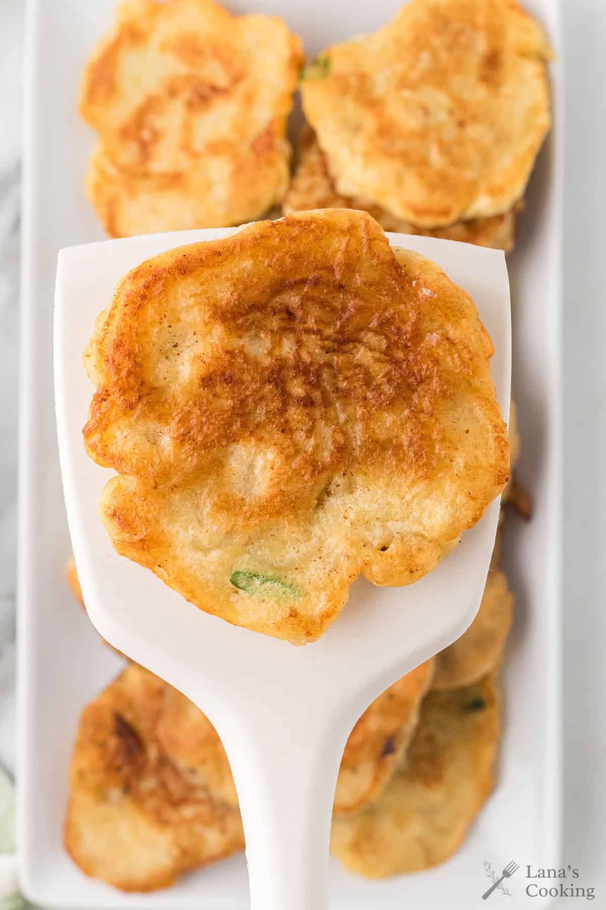 A white spatula holding one potato pancake.