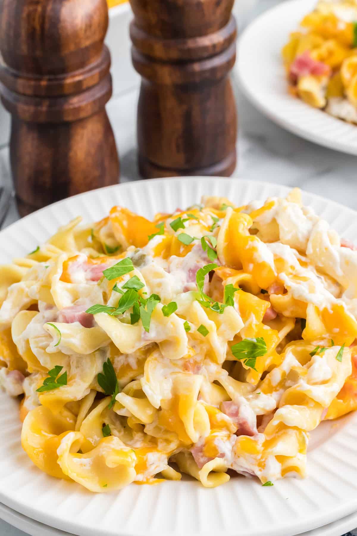 A plate of cheesy pasta with ham, garnished with fresh parsley, sits on a white plate.