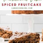 A slice of spiced fruitcake with powdered sugar on a plate, with more cake on a white stand in the background.