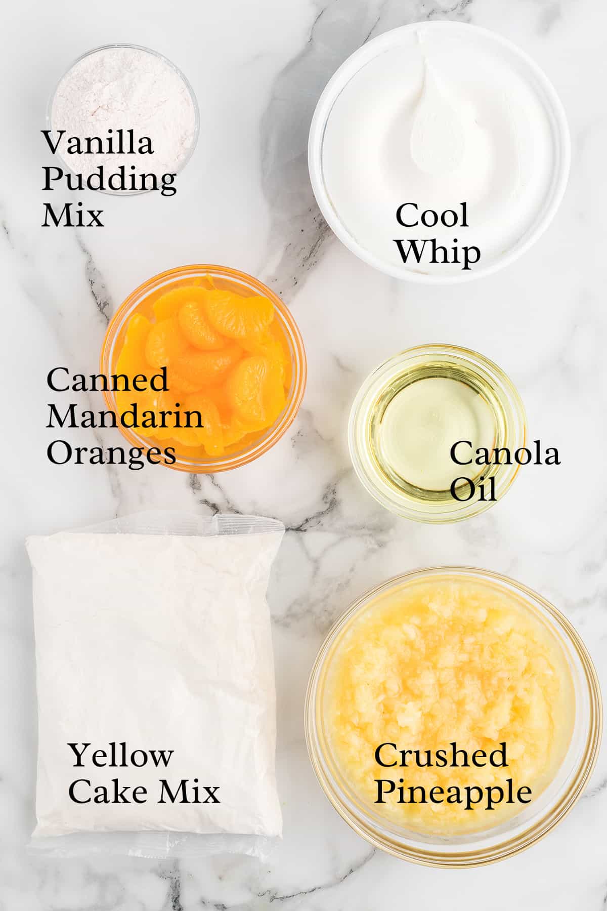 Six labeled bowls containing vanilla pudding mix, Cool Whip, canned mandarin oranges, canola oil, yellow cake mix, and crushed pineapple.